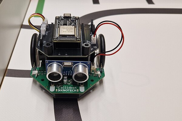 ähnliche einem Miniaturauto auf einem Mikrocontroller mit Kameraaugen und Kabeln, fährt auf einer schwarzen Linie auf einem Tisch oder Untergrund lang